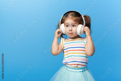 Happy smiling child enjoys listens to music in headphones over colorful bleu background. Vivid and fun emotions, happy child with pleasure listens to songs in wireless headphones photo