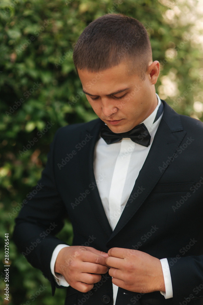 Young man walking in the park. Handsome groom in black suit Young man walking in the park. Handsome groom in black suit