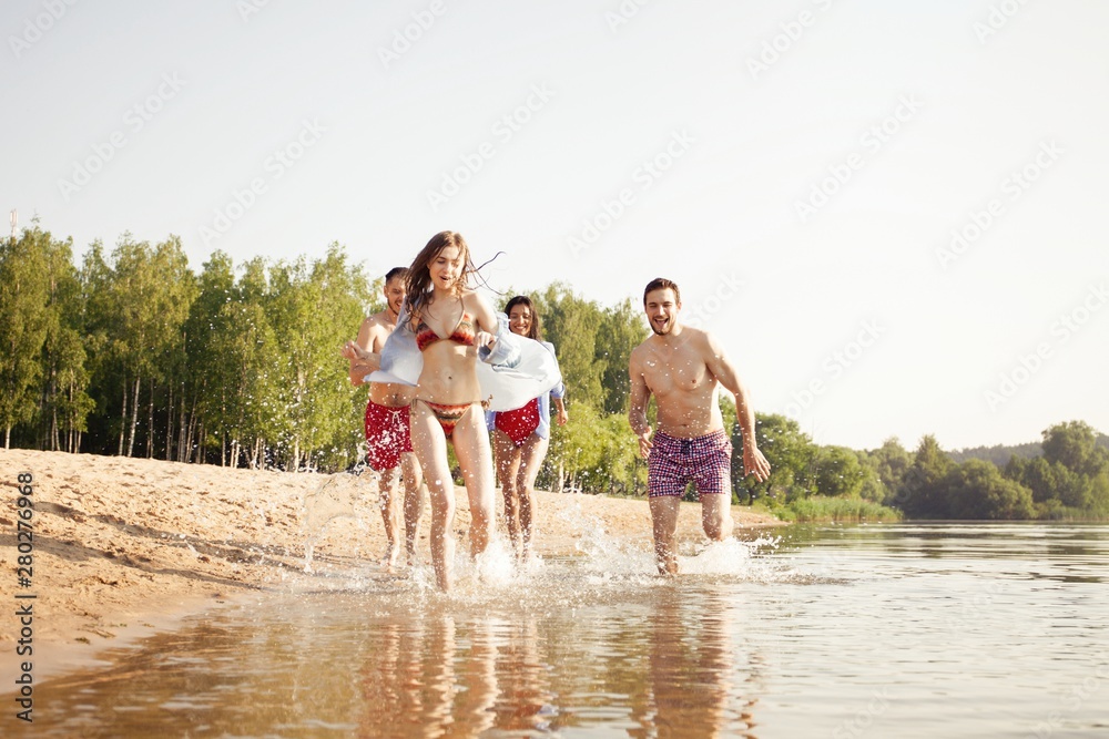 Group of happy friends running in to water - active people having fun on the beach on vacation Group of happy friends running in to water - active people having fun on the beach on vacation