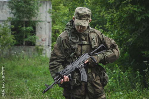 military in full uniform is in the woods holding a Kalashnikov