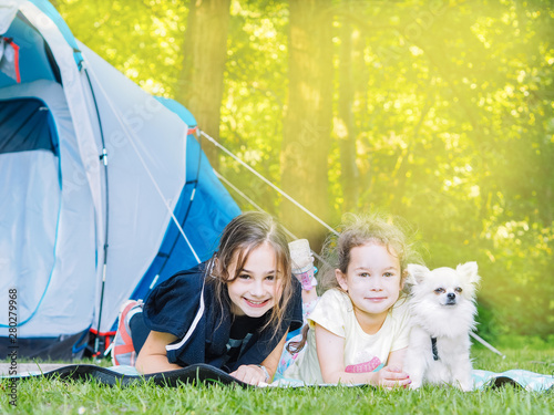 Camp in the tent - girls with little dog chihuahua sitting together near the tent. Camping with children. Camping tourism and vacation concept