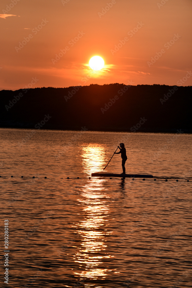 Person using a sup in the sunset.