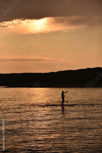 Person using a sup in the sunset.