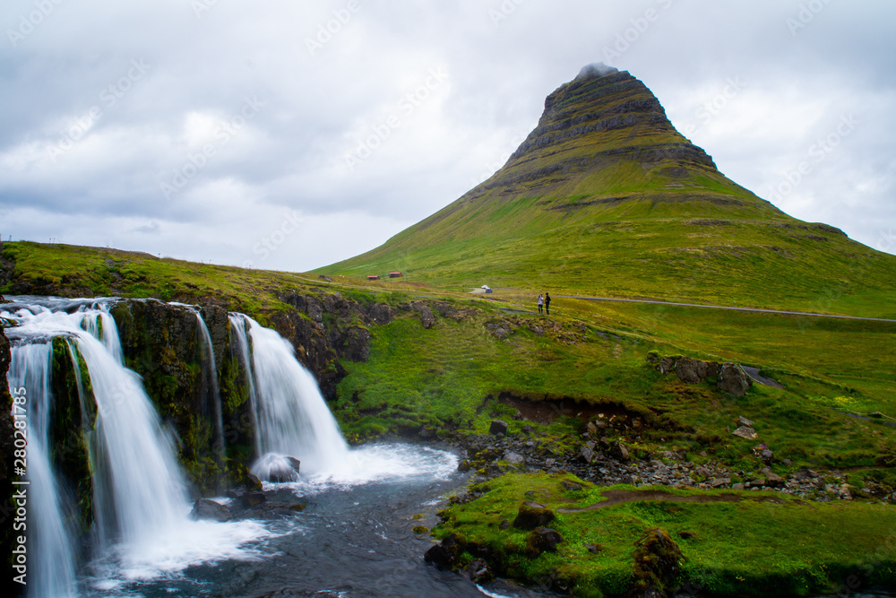 Fototapeta premium Scenic panorama view of long exposure falling water in front of Kirkjufell volcano mountain, the most iconic travel destination location in Iceland. Summer time.