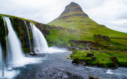 Scenic panorama view of long exposure falling water in front of Kirkjufell volcano mountain, the most iconic travel destination location in Iceland. Summer time.