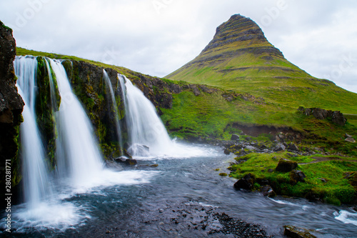Scenic panorama view of long exposure falling water in front of Kirkjufell volcano mountain  the most iconic travel destination location in Iceland. Summer time.
