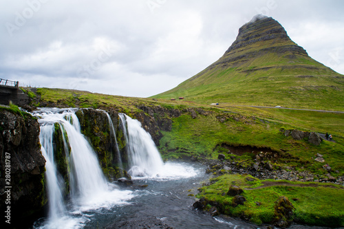 Scenic panorama view of long exposure falling water in front of Kirkjufell volcano mountain, the most iconic travel destination location in Iceland. Summer time.