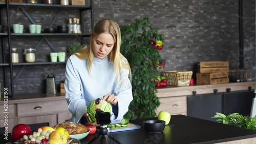 Young beautiful blonde takes on videos as she cooks in the kitchen photo