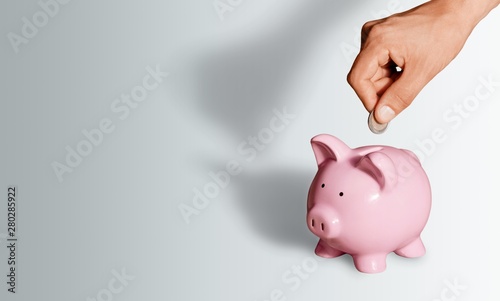Hand putting coin to piggy bank on blue background