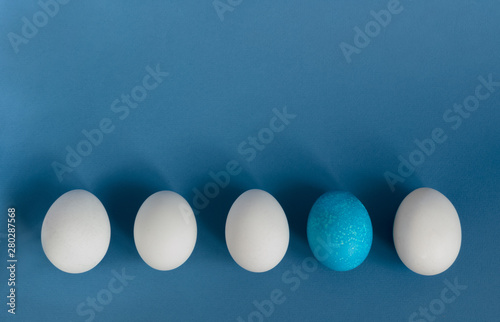 White eggs and blue egg in a row on blue background
