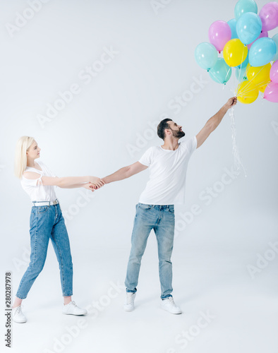 beautiful girl holding hand of handsome man with balloons on grey