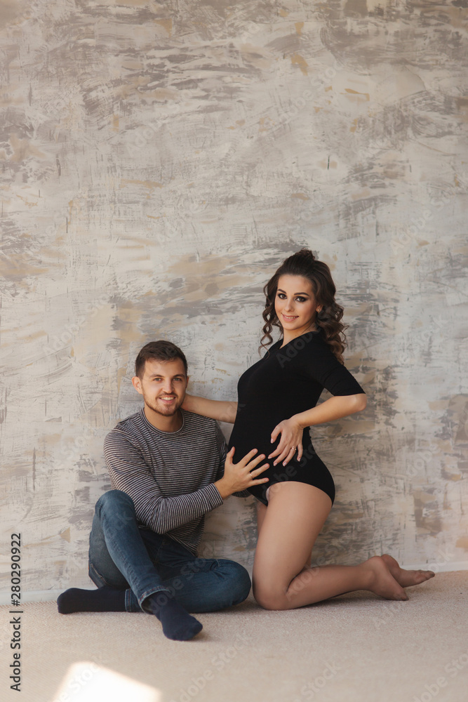Happy man put his handr on the belly of his pregnant wife. Young family in studio. Couple wait for a baby
