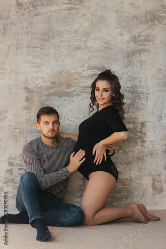 Happy man put his handr on the belly of his pregnant wife. Young family in studio. Couple wait for a baby