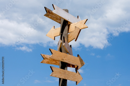 Multiple blank wooden arrow signposts on wood  pole agains blue sky  .