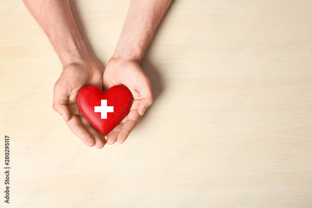 Man holding red heart on light wooden background, top view with space for text. Donation concept Man holding red heart on light wooden background, top view with space for text. Donation concept