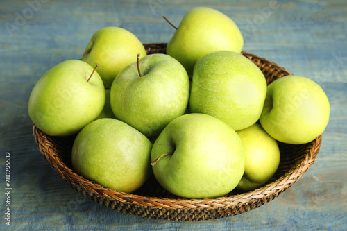 Wicker bowl of fresh ripe green apples on blue wooden table
