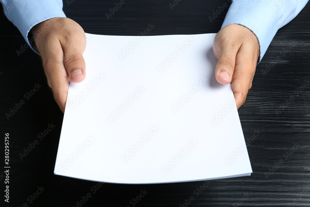 Man holding blank paper sheets for brochure at black wooden table. Mock up