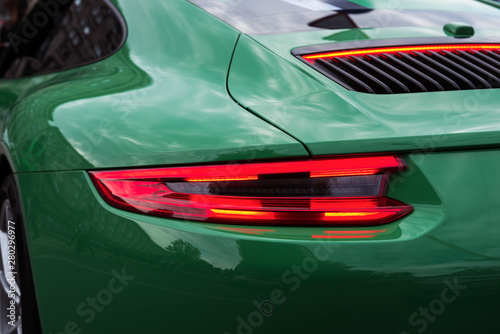 Green sports car with red backlight on. Closeup of a luxury car body. Modern LED light. Rear light strip.