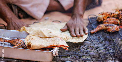 Canvas-taulu Bedouin Man cooks chicken and flat bread on a grill outside.