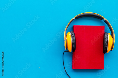 Books with headphones for listening to audiobook on blue background top view copy space