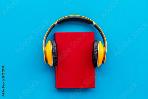 Books with headphones for listening to audiobook on blue background top view copy space