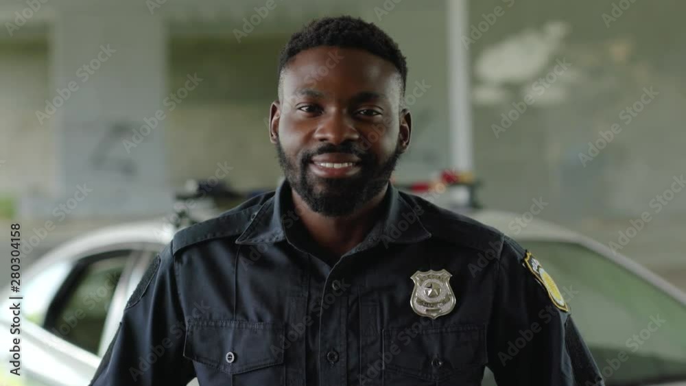 Smiling face african american young man cops stand near patrol car look at camera enforcement happy officer police uniform auto safety security communication control policeman portrait slow motion