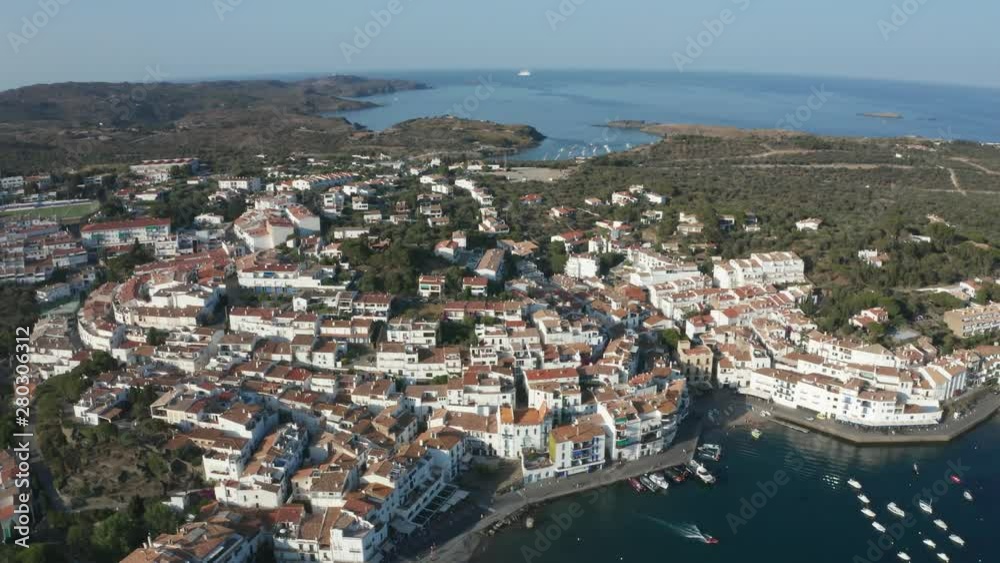 Aerial view of tiled roofs, narrow streets, white houses of resort coastal town Cadaques on Cap de Creus peninsula. Drone shot of boats and yachts anchored in bay on background of scenic cityscape Aerial view of tiled roofs, narrow streets, white houses of resort coastal town Cadaques on Cap de Creus peninsula. Drone shot of boats and yachts anchored in bay on background of scenic cityscape