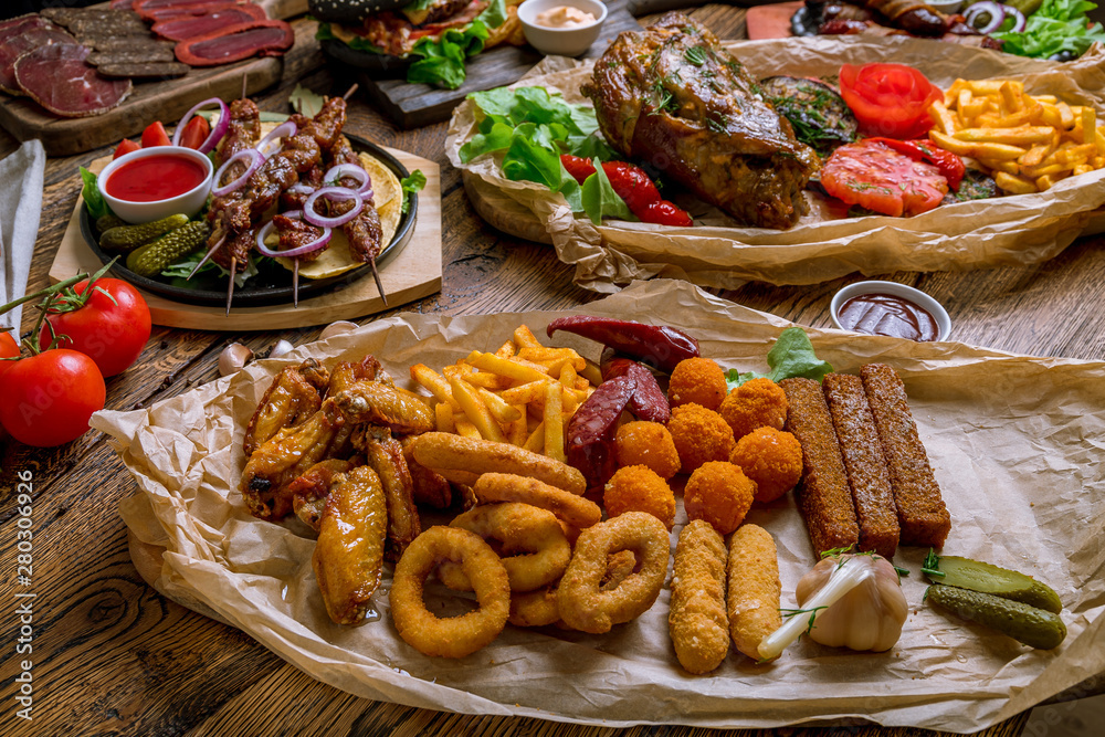Still life, assorted beer snacks, kebabs skewers, black burger with meat, meat slices on wooden table