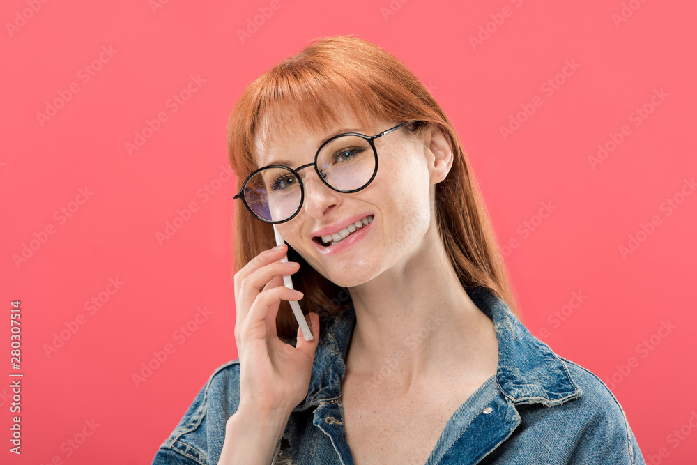 attractive redhead girl in glasses and denim jacket talking on smartphone isolated on pink attractive redhead girl in glasses and denim jacket talking on smartphone isolated on pink