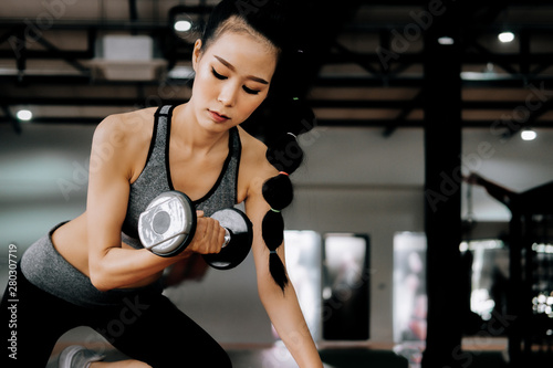 Fototapeta Naklejka Na Ścianę i Meble -  sport woman at fitness gym club doing exercise for arms with dumbbells and showing muscle bodybuilding, fitness concept, sport concept