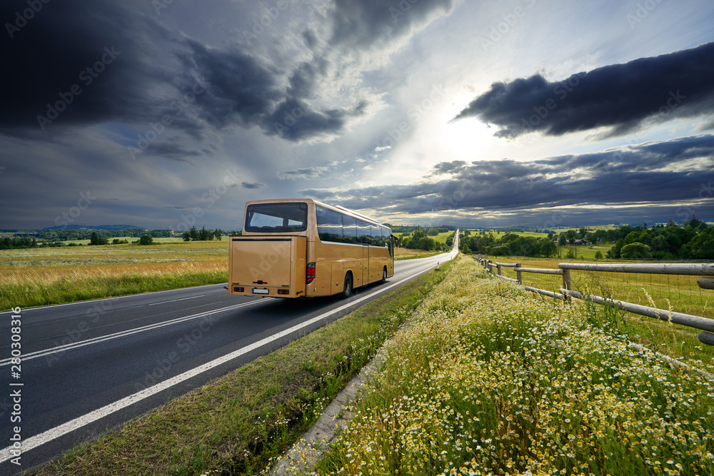 Bus traveling on the asphalt road in rural landscape at sunset with dramatic clouds
