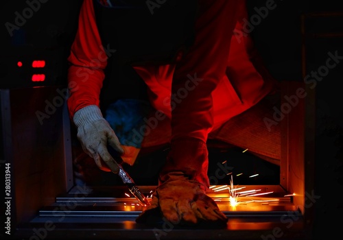 A woman wearing a pink long sleeve jacket, welding mask and leather gloves, welding a metal case for computer server rack, with sparks