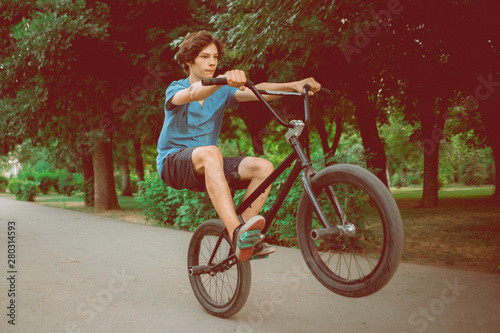 young man riding on a bmx bike on a back rear wheel, doing tricks in the city