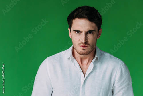 front view of angry man in white shirt looking at camera isolated on green