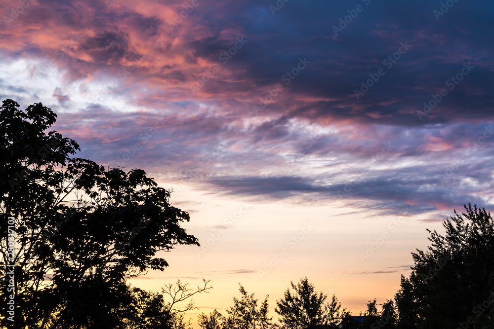 Beautiful sky with colorful clouds at sunset and silhouettes of trees.
