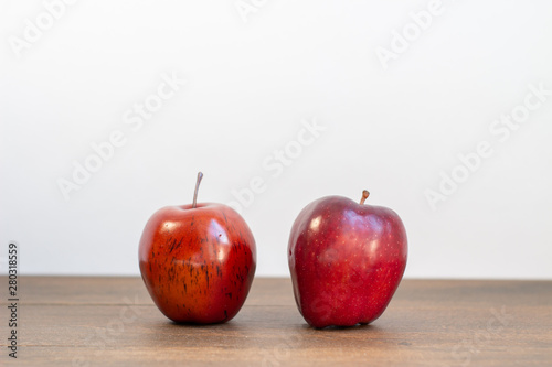A fake red delicious and real apple next to each other on a white background