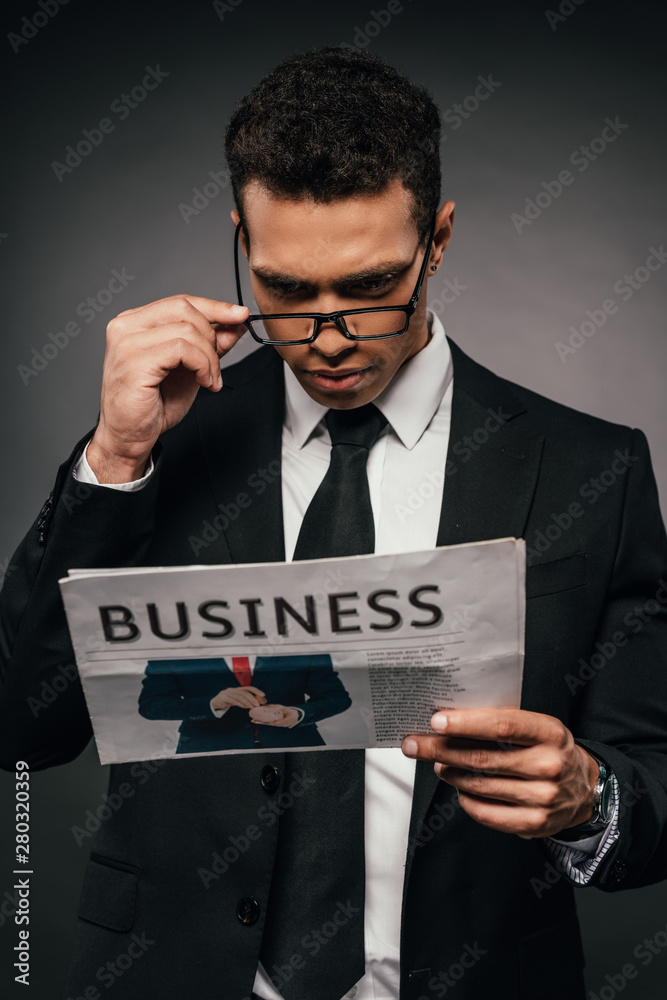 african american businessman in glasses reading business newspaper on dark background african american businessman in glasses reading business newspaper on dark background