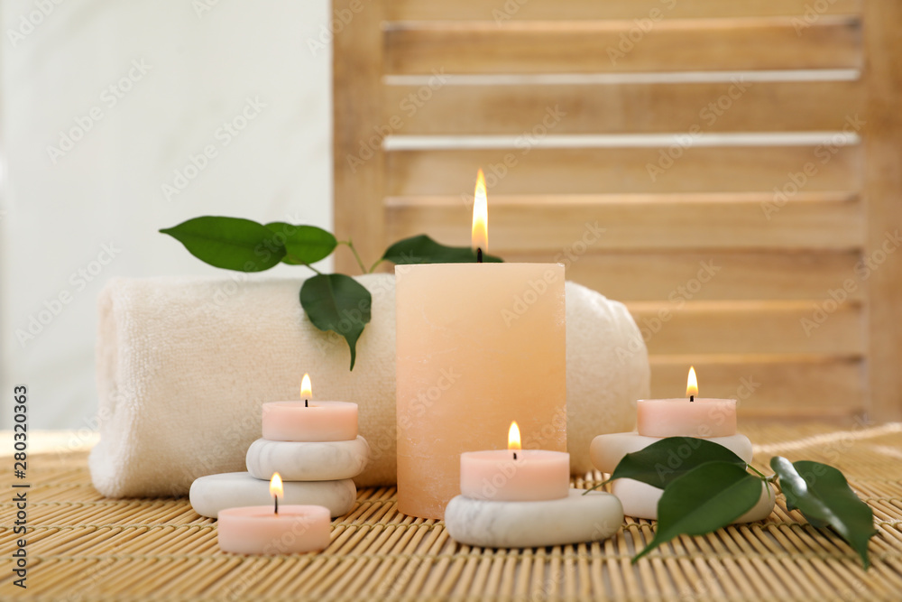 Composition of spa stones, towel and burning candles on bamboo mat