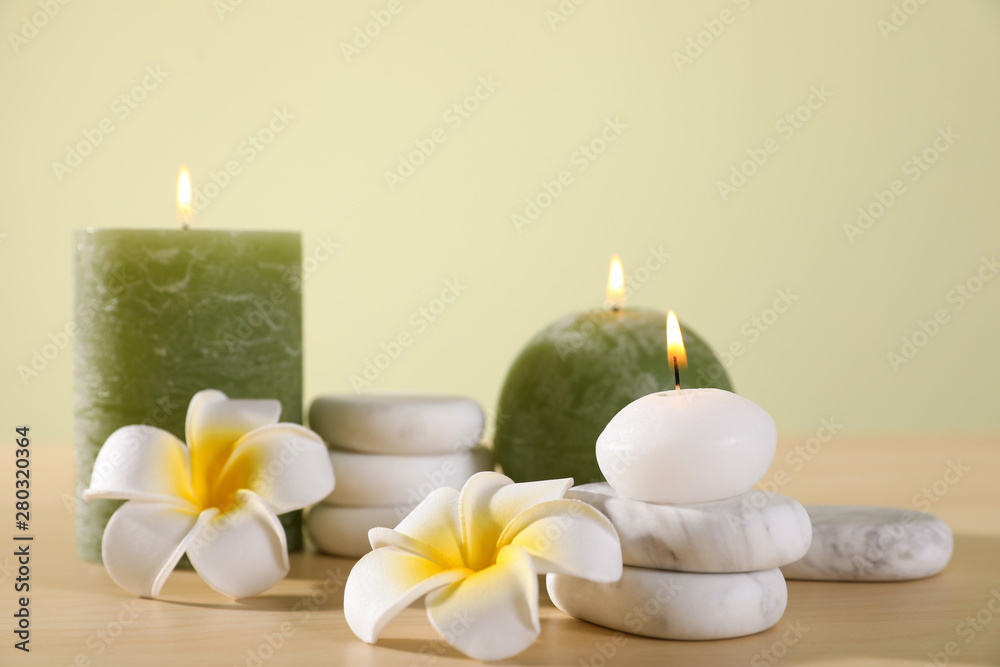 Composition of spa stones, flowers and burning candles on wooden table against light green background