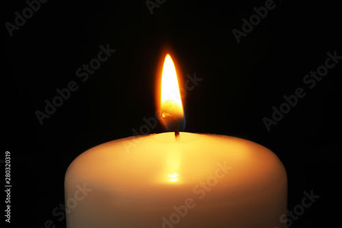 Burning candle on dark background, closeup. Symbol of sorrow