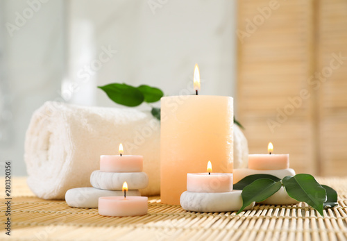 Composition of spa stones, towel and burning candles on bamboo mat