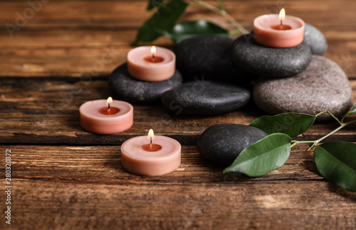 Composition of spa stones  green leaves and burning candles on wooden table