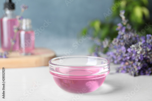 Bowl of lavender essential oil on white wooden table against blue background. Space for text © New Africa