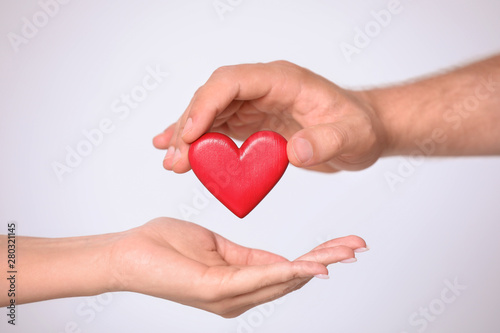 Man giving red heart to woman on white background  closeup. Donation concept