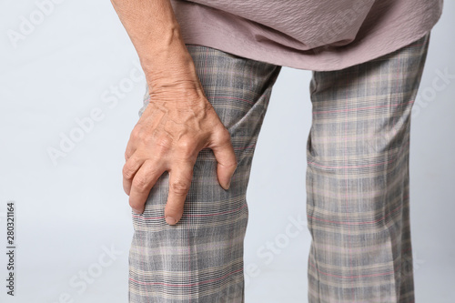 Senior woman having knee problems on grey background, closeup