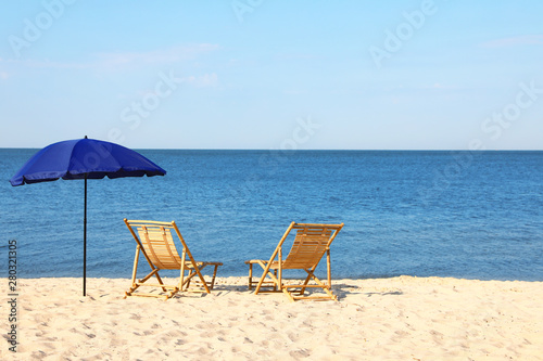 Empty wooden sunbeds and umbrella on sandy shore. Beach accessories © New Africa