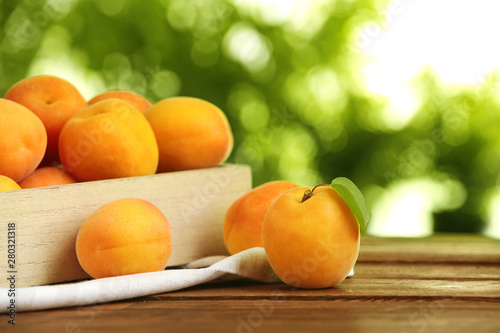 Crate and delicious ripe sweet apricots on wooden table against blurred background  space for text