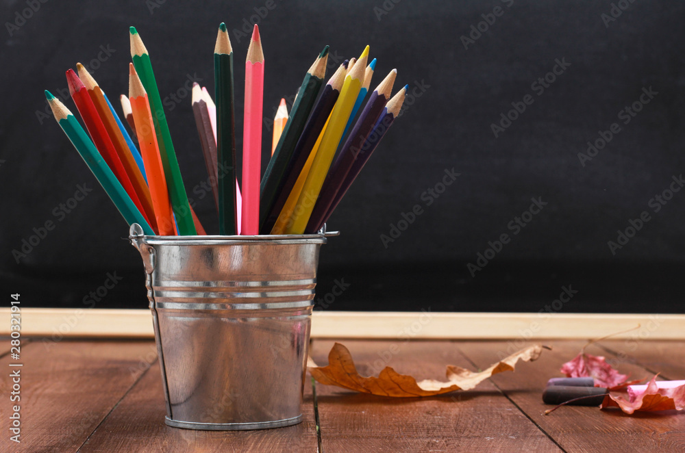 Colored pencils, crayons and fall leaves on wooden table. Black chalk board in background. Back to school, September, education concept.