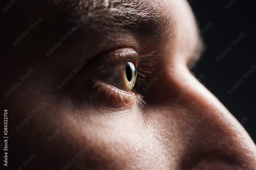 close up view of adult man eye with eyelashes and eyebrow looking away in dark