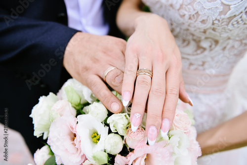 A newly weding couple place their hands on a wedding bouquet showing off their wedding rings.